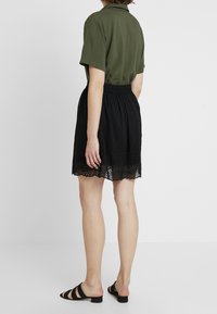 Grön kortärmad skjorta och svart kjol med broderad fåll. Kjolen har en rynkad midja och en lager-på-lager, texturerad finish.