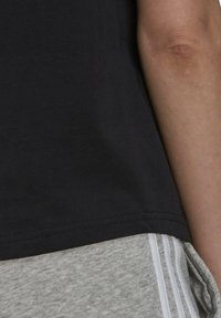 Svart bomullströja med en slät textur, som har en rund halsringning och korta ärmar, tillsammans med ljusgråa träningsshorts med vita ränder.