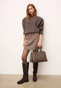 Brūns vilnas džemperis, beigu svārki, brūni ceļgala zābaki ar zelta akcentiem un atbilstoša brūna rokassoma. Gludās tekstūras un vienkāršās līnijas.