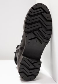 Suola nera di stivale con profilo di battistrada zigzag profondo, taglia 37 contrassegnata, inclinata contro uno sfondo bianco con angoli.