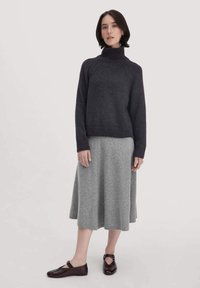 Dunkelgrauer gestrickter Rollkragenpullover mit geripptem Saum, kombiniert mit einem hellgrauen, knielangen, ausgestellten Rock. Schuhwerk: dunkelbraune Mary Jane Schuhe.