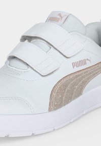 Λευκό αθλητικό παπούτσι Puma με δύο λουριά βέλκρο και μια λαμπερή μπεζ λωρίδα λογότυπου Puma στο πλάι.