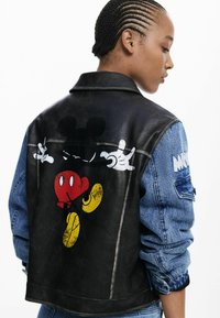 Black leather jacket with denim sleeves, featuring a colorful Mickey Mouse graphic on the back. Includes details like textured fabric and visible stitching.
