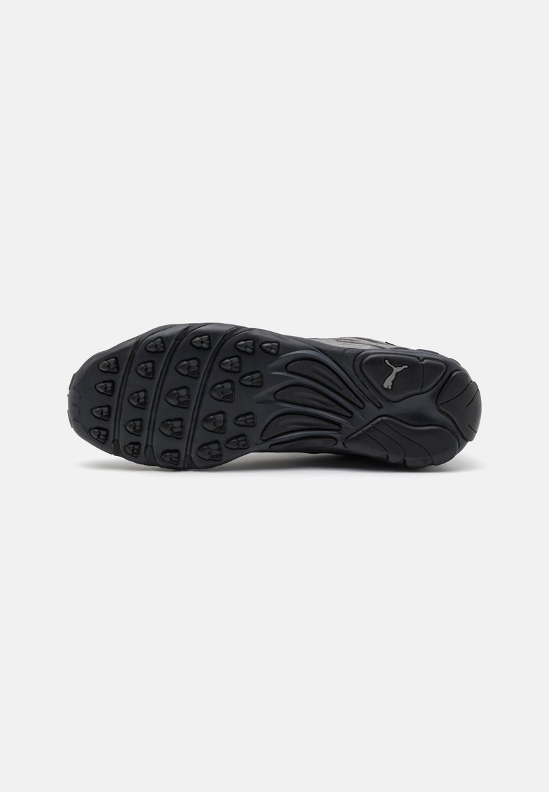 Schwarze Turnschuhsohle aus strukturiertem Gummi für besseren Halt, mit Mustern, die Krallen ähneln, und einem silbernen Puma-Logo an der Seite.