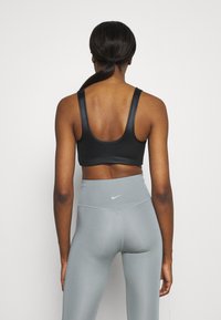 Soutien-gorge de sport noir avec un dos en scoop et leggings taille haute gris avec un petit logo Nike blanc sur la ceinture. Texture de tissu lisse.