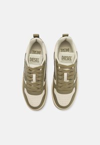 Green and beige sneakers with a textured fabric upper, perforated toe box, logo on tongue, and contrasting accents along the sides.