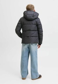 Mörkgrå puffjacka med huva, med en quiltad design och elastiska ärmslut, i kombination med ljusblå vida jeans och bruna skor.