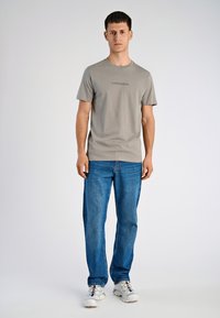 Szara bawełniana koszulka z krótkim rękawem i okrągłym dekoltem, z delikatnym nadrukiem logo. W zestawie z niebieskimi dżinsami i białymi trampkami.