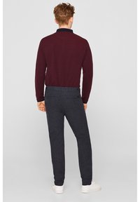 Burgundy long-sleeve collared shirt paired with dark textured trousers and white sneakers; view from the back showcasing the outfit.