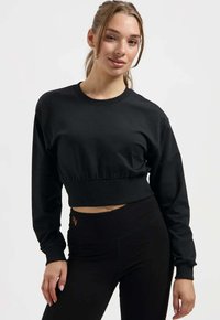 Schwarzes, kurz geschnittenes Sweatshirt mit langen Ärmeln, geripptem Halsausschnitt und Bund. Der Stoff wirkt glatt und weich und ergänzt die hoch taillierten schwarzen Leggings.