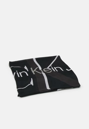 Sort foldet stof med hvidt og gråt Calvin Klein-logo og bogstaver på en ensartet lys baggrund.