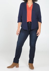 Cárdigan de punto en navy, blusa roja con patrón blanco, vaqueros oscuros y botas de tobillo color beige. El cárdigan tiene un frente abierto y mangas 3/4.