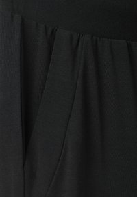 Falda negra con una tela suave y texturizada, con detalles plisados en la cintura. El diseño es holgado y fluye suavemente.