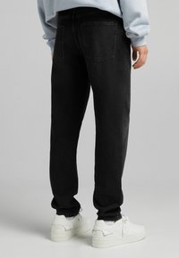 Mustat farkut, joissa on suora lahje ja klassinen viisi-taskumalli. Yhdistetty valkoisiin lenkkareihin ja vaaleansiniseen huppariin.