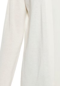 Cardigan a maniche lunghe di un leggero beige, realizzato in morbido tessuto a maglia, con un taglio dritto e un sottile dettaglio delle cuciture laterali.