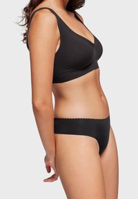 Zwarte draadloze bh met een gladde textuur en een V-halsontwerp, gecombineerd met bijpassende zwarte low-rise slips met een geschulpte rand.