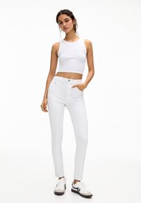 Fehér crop top, amelyet fehér skinny farmernadrággal párosítottak. Az öltözet sima textúrájú, testhezálló fazonú és minimalista kiegészítőkkel rendelkezik.