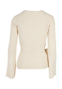 Beige ribbad långärmad topp med en figursydd design, breda trumpetärmar och en knytning vid midjan. Texturerat tyg ger visuell intress.