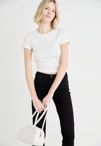 Vit, figurnära t-shirt med korta ärmar, ihopparad med svarta jeans. Modellen håller en liten vit handväska med en strukturerad form och två handtag.