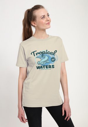 T-shirt beige in cotone con una stampa grafica di uno squalo martello e testo che dice "Acque Tropicali" in verde scuro e blu.