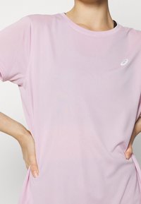 Camiseta deportiva de color rosa claro con mangas cortas, escote redondo y tela texturizada. Presenta un pequeño logo blanco en el pecho.
