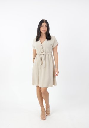 Ärmeloses Kleid in Beige, aus einem leichten Stoff gefertigt, mit V-Ausschnitt, Knopfverschluss und einer gebundenen Taille für eine anpassbare Passform.