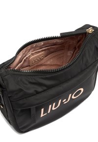 Borsa nera in nylon con chiusura a zip, dotata di un logo rosa sul davanti e una texture liscia. All'interno presenta una fodera con motivo e una tasca in rete.