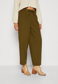 Pantalons décontractés vert olive avec une taille élastique et un cordon de serrage, associés à des bottes à talons texturées beige.