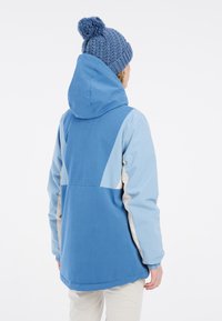 Giacca con cappuccio blu con accenti di blu chiaro e crema; presenta una texture morbida, un design casual e polsini elasticizzati. Adatta per l'uso all'aperto.