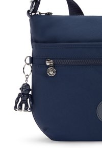 Borsa in nylon blu navy con una superficie liscia, dotata di una tasca con zip e un portachiavi con una piccola figura nera attaccata.