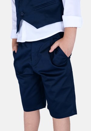 Pantaloni corti blu navy realizzati in tessuto morbido, dotati di tasche laterali e una vestibilità su misura, indossati con una camicia bianca con colletto e gilet.