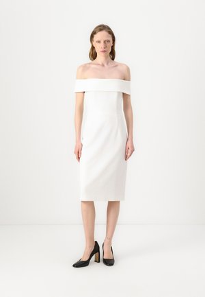 Witte off-shoulder jurk met een aansluitende snit, knielange zoom en gladde stof. Draag met zwarte hoge hakken.