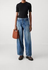 Svart åtsittande t-shirt, blåvida jeans, bruna kängor med kraftig sula och en liten brun handväska med ett handtag upptill.