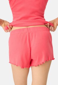 Korte roze fleece shorts met een golvende zoom, voorzien van een elastische tailleband voor comfort. De stof lijkt zacht en glad te zijn.
