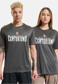 Pilkos sportinės marškinėliai, pagaminti iš lygios medžiagos, su "Cologne Centurions" baltu spaudiniu ir mažo logotipo akcentu krūtinėje.
