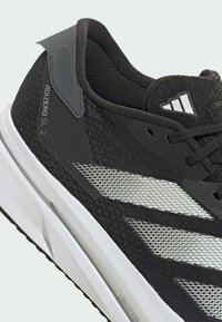 Fekete sportcipő, légáteresztő hálós felsőrésszel, szintetikus elemekkel, fényvisszaverő ezüst csíkokkal és fehér középtalppal, amelyen a "Lightstrike" felirat található.