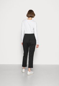 Zwarte tapered broek met een gladde textuur, hoge taille en zijzakken. Gecombineerd met een wit langoverhemd en witte sneakers.