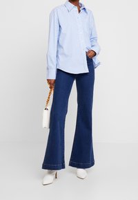 Blauw-wit gestreept overhemd met knopen, gecombineerd met donker uitlopende spijkerbroek. Witte pumps en een kleine witte handtas met een kettingriem.