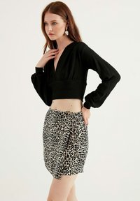 Schwarzes Cropped-Top mit langen Ärmeln, kombiniert mit einem Rock im Leopardenmuster, der eine vordere Bindeschnur hat. Strukturierter Stoff, elegantes Design.