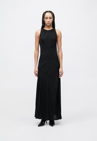 Vestido maxi preto sem mangas com silhueta justa, apresentando um decote alto e uma fenda lateral. Feito de tecido leve e fluido.