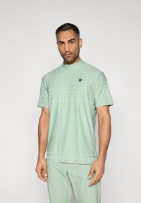 Μέντα πράσινο κοντομάνικο μπλουζάκι με ψηλό γιακά, που διαθέτει διακριτικό γεωμετρικό μοτίβο και μικρό λογότυπο στο αριστερό στήθος.