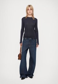 Dark long-sleeve top paired with loose, wide-leg, dark blue jeans. Model holds a small brown handbag. Simple, fitted design with smooth texture.