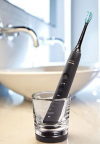 Spazzolino elettrico sonico con manico nero, setole blu e verdi, posizionato in un bicchiere trasparente su una superficie di marmo.