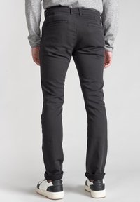 Maglietta grigia a maniche lunghe, pantaloni neri slim-fit e sneakers bianche con dettagli neri. I pantaloni presentano tasche posteriori e una texture liscia.