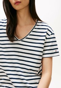 Camiseta a rayas con rayas horizontales en azul marino y blanco, diseño de cuello en v, mangas cortas y un pequeño logotipo en la manga.