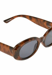 Lunettes de soleil en écaille de tortue avec des verres ovales, des montures épaisses et une finition brillante. Les branches présentent une courbe subtile et affichent une marque discrète.