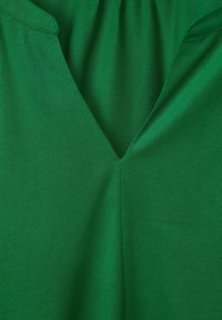 Grön V-ringad plagg med ett slätt, texturerat tyg. Har en avslappnad passform och subtil sömnad längs kragen och sömmarna.