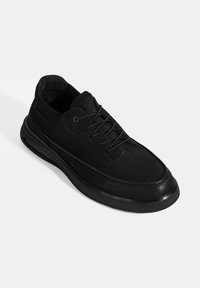 Black sneaker made of suede with a smooth texture, featuring round laces, a padded collar, and a thick rubber sole with a sleek design.