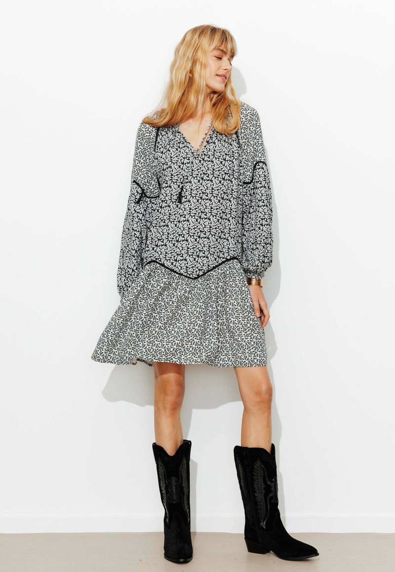 Robe florale noir et blanc avec une jupe évasée, des manches longues et un passepoil noir contrastant, accompagnée de bottes de cowboy noires.