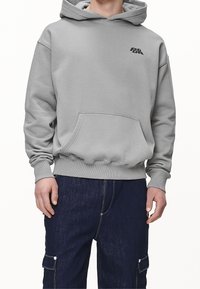Szara bluza z kapturem wykonana z miękkiej tkaniny, z przednią kieszenią i małym czarnym logo na piersi. Mankiety i dół wykończone ściągaczami.